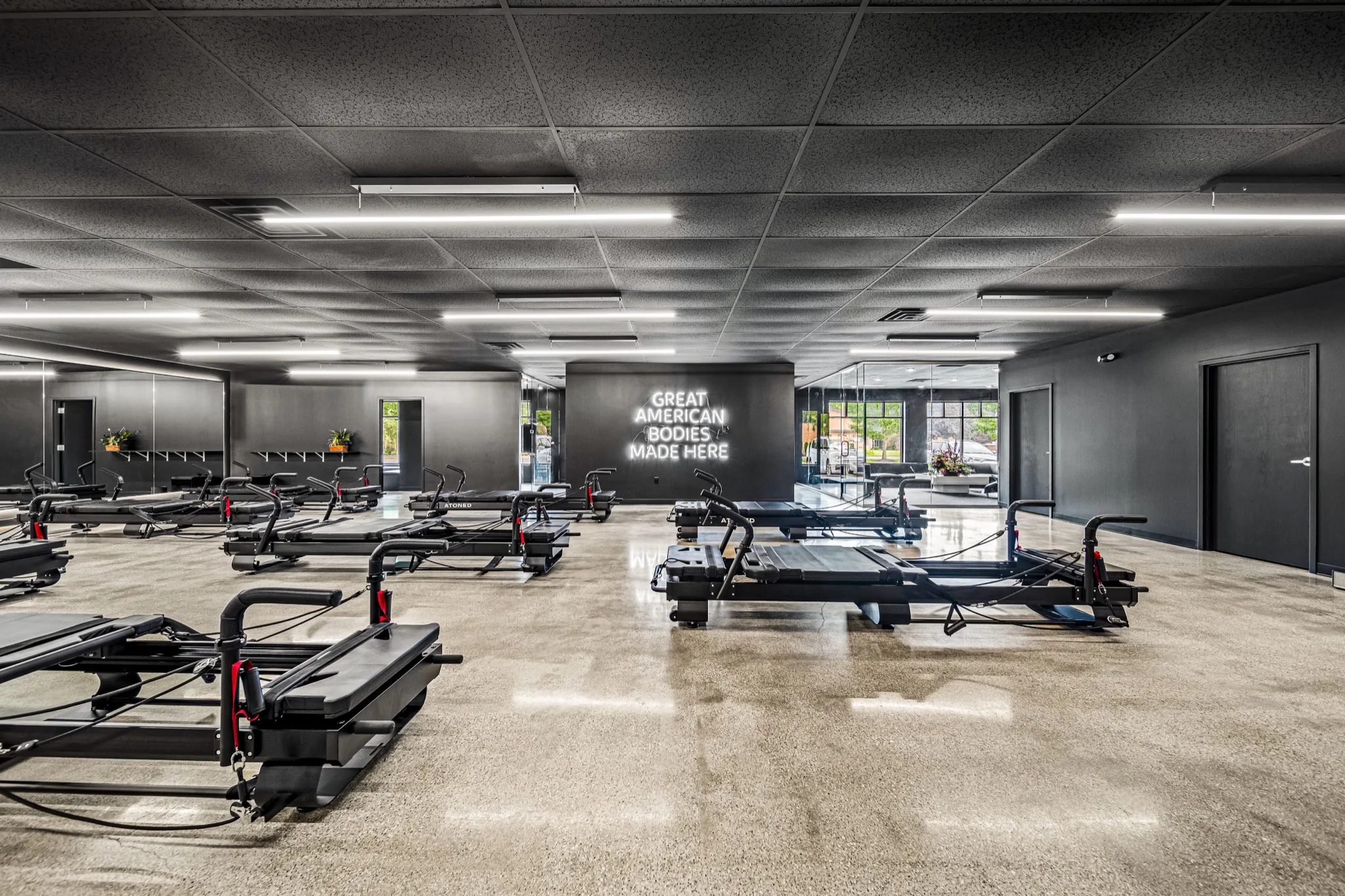 Premium Pilates studio floor with rows of reformers, neon wall art, and mirrored walls — commercial fitness construction by Skoda Construction, Northeast Ohio