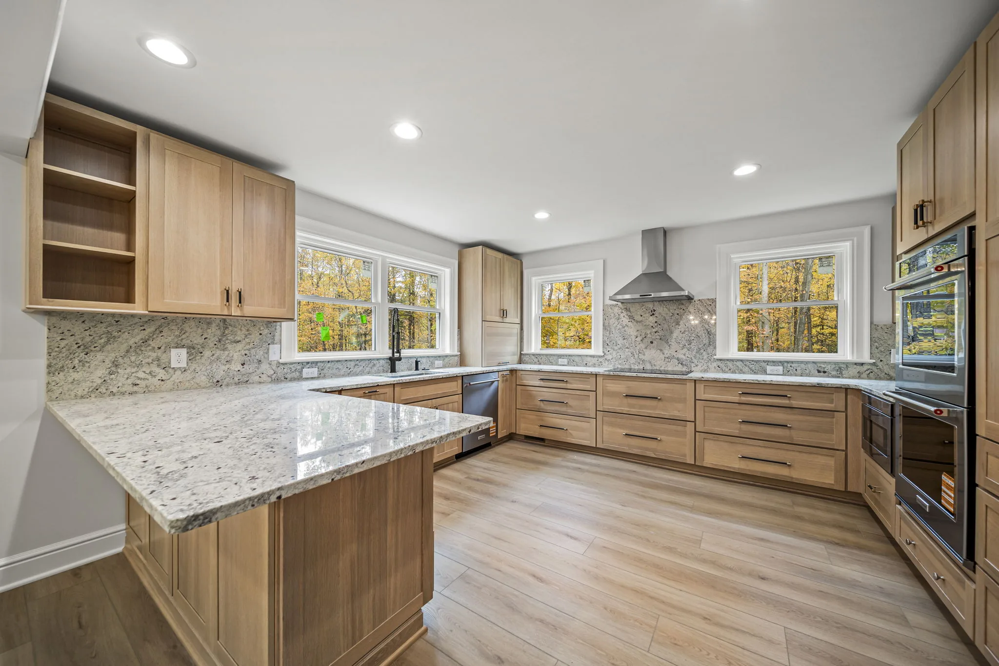 Natural white oak kitchen with granite countertops and wooded views through picture windows — custom home by Skoda Construction, Northeast Ohio