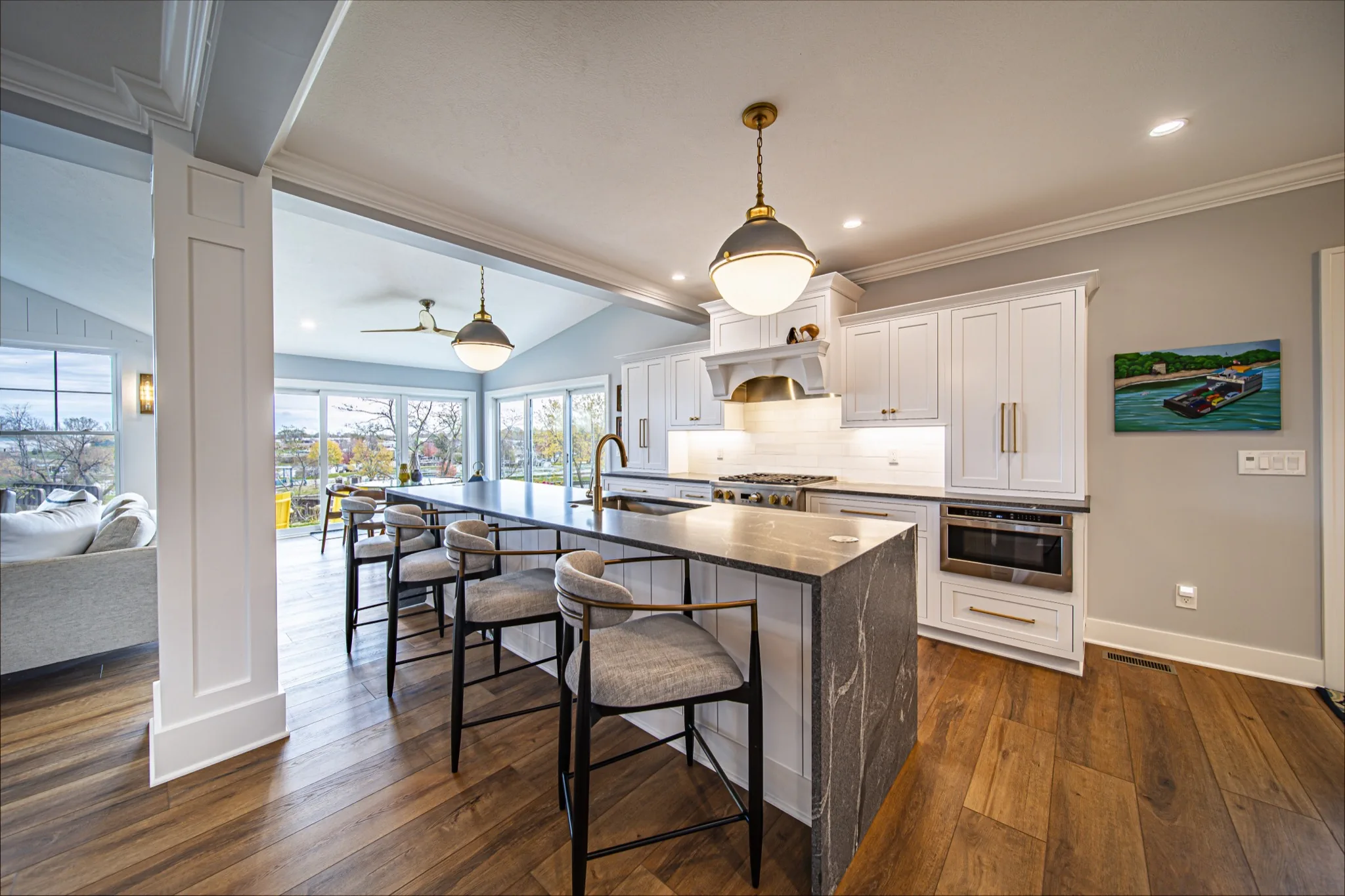 White kitchen with dark marble island, upholstered bar stools, and brass fixtures in open-concept farmhouse — Skoda Construction, Northeast Ohio