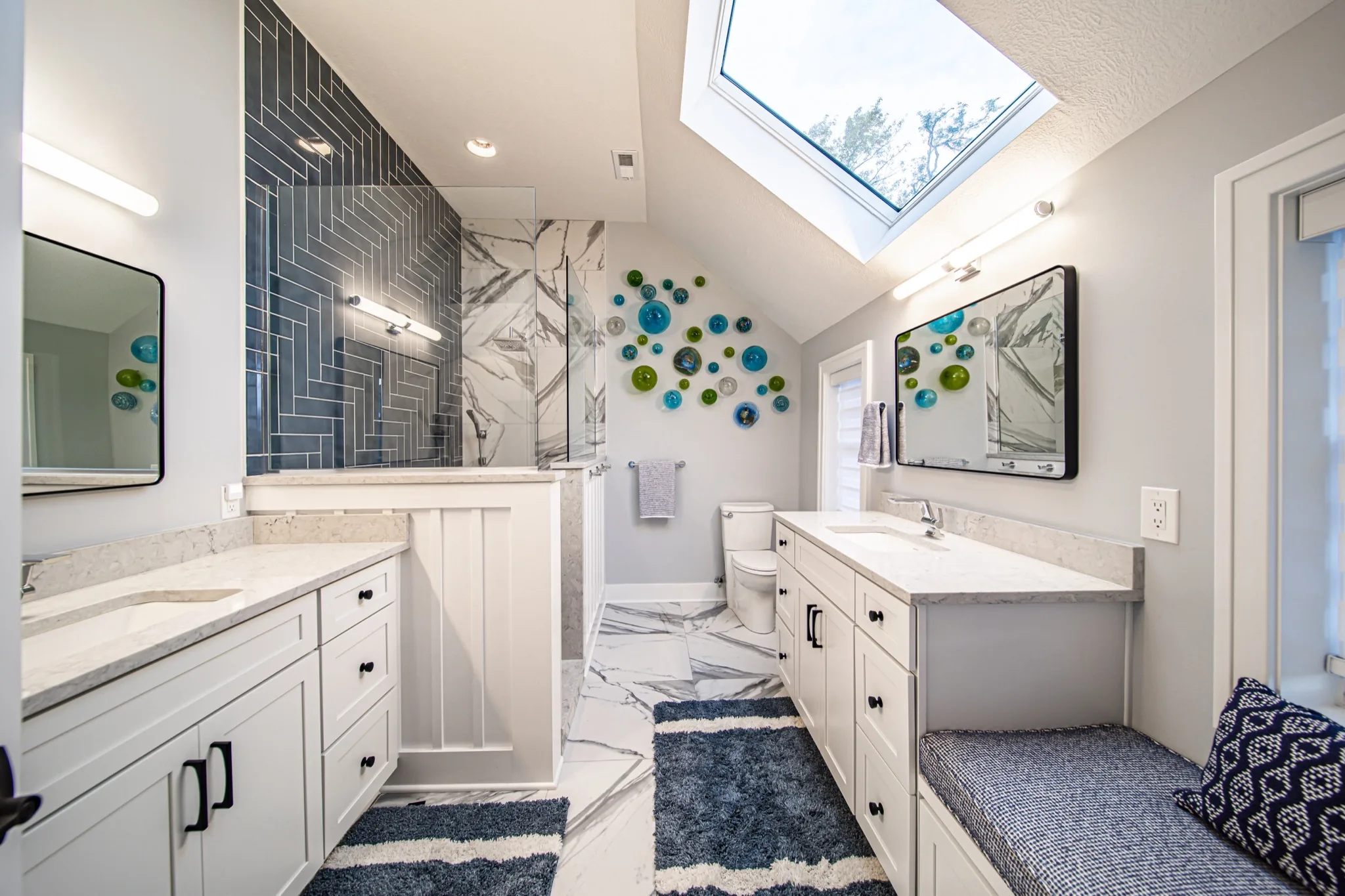 Luxury primary bathroom with dual vanities, skylight, blue herringbone tile, and marble walk-in shower — Skoda Construction, Northeast Ohio