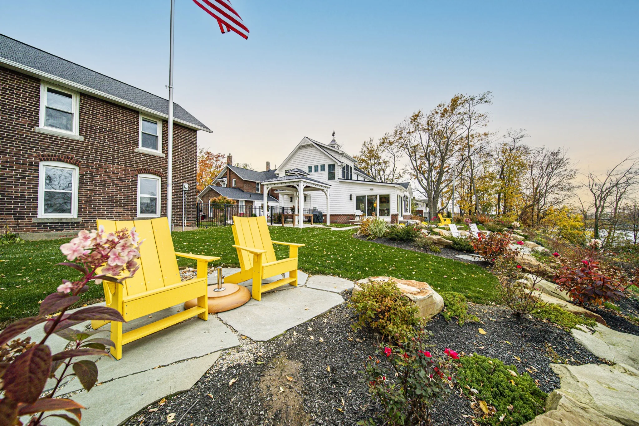 Custom property overview with Adirondack seating, stone landscaping, and white farmhouse — Skoda Construction, Northeast Ohio
