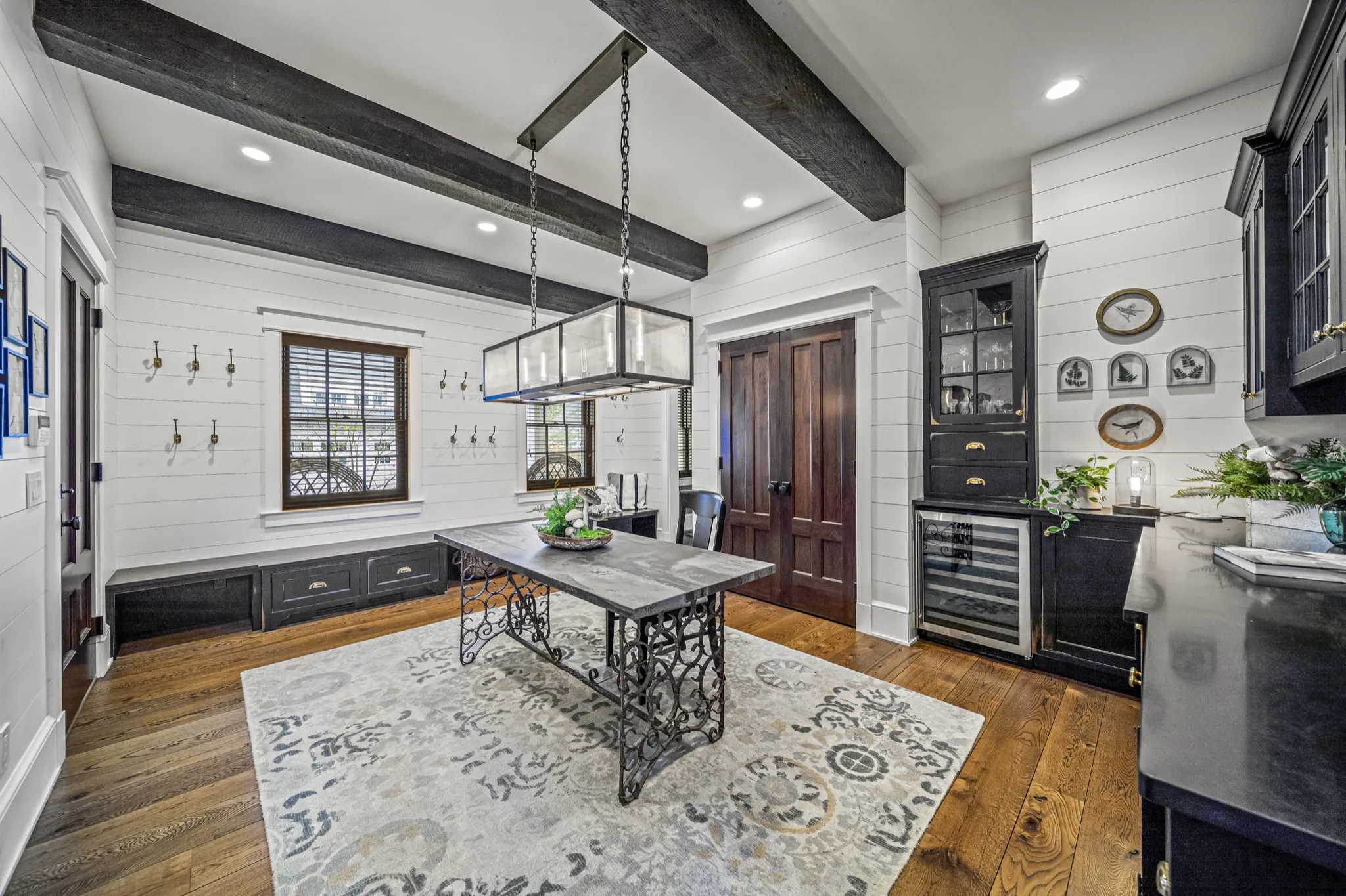 Rustic breakfast nook with dark timber ceiling beams, industrial lantern chandelier, wrought-iron table, built-in bench, and wine cooler — custom farmhouse by Skoda Construction, Northeast Ohio