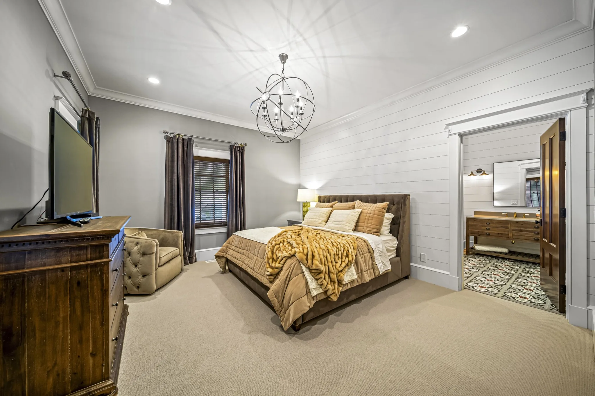 Guest bedroom with iron orb chandelier, shiplap ceiling, reclaimed wood furniture, and doorway to patterned tile bathroom — luxury custom home by Skoda Construction, Northeast Ohio