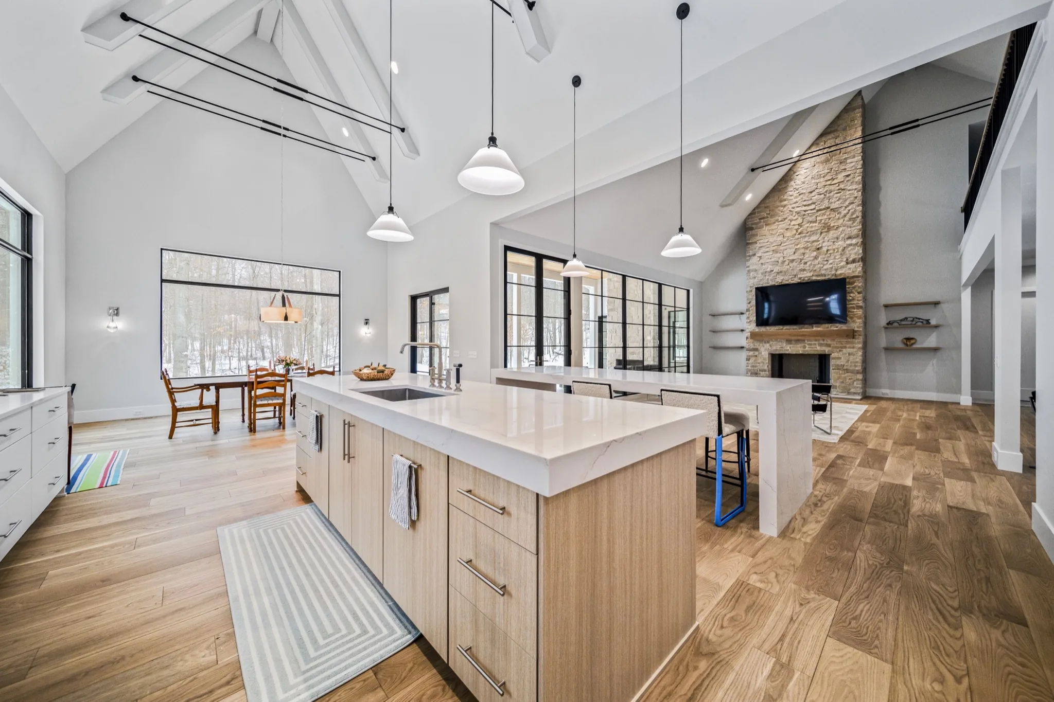 Open-concept luxury kitchen with dual islands, waterfall quartz countertops, pendant lighting, and soaring cathedral ceiling with exposed beams — custom home by Skoda Construction, Northeast Ohio