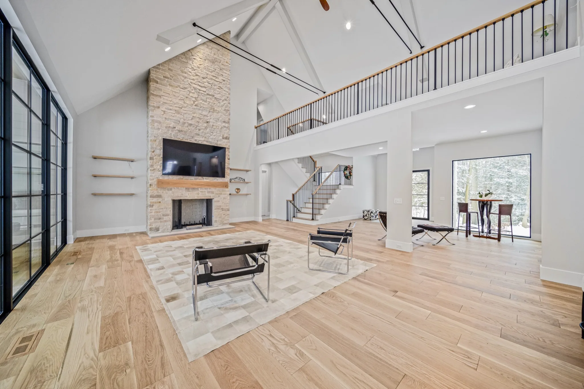 Floor-to-ceiling natural stone fireplace with floating wood mantel in a soaring two-story great room with modern iron loft railing — luxury custom home by Skoda Construction