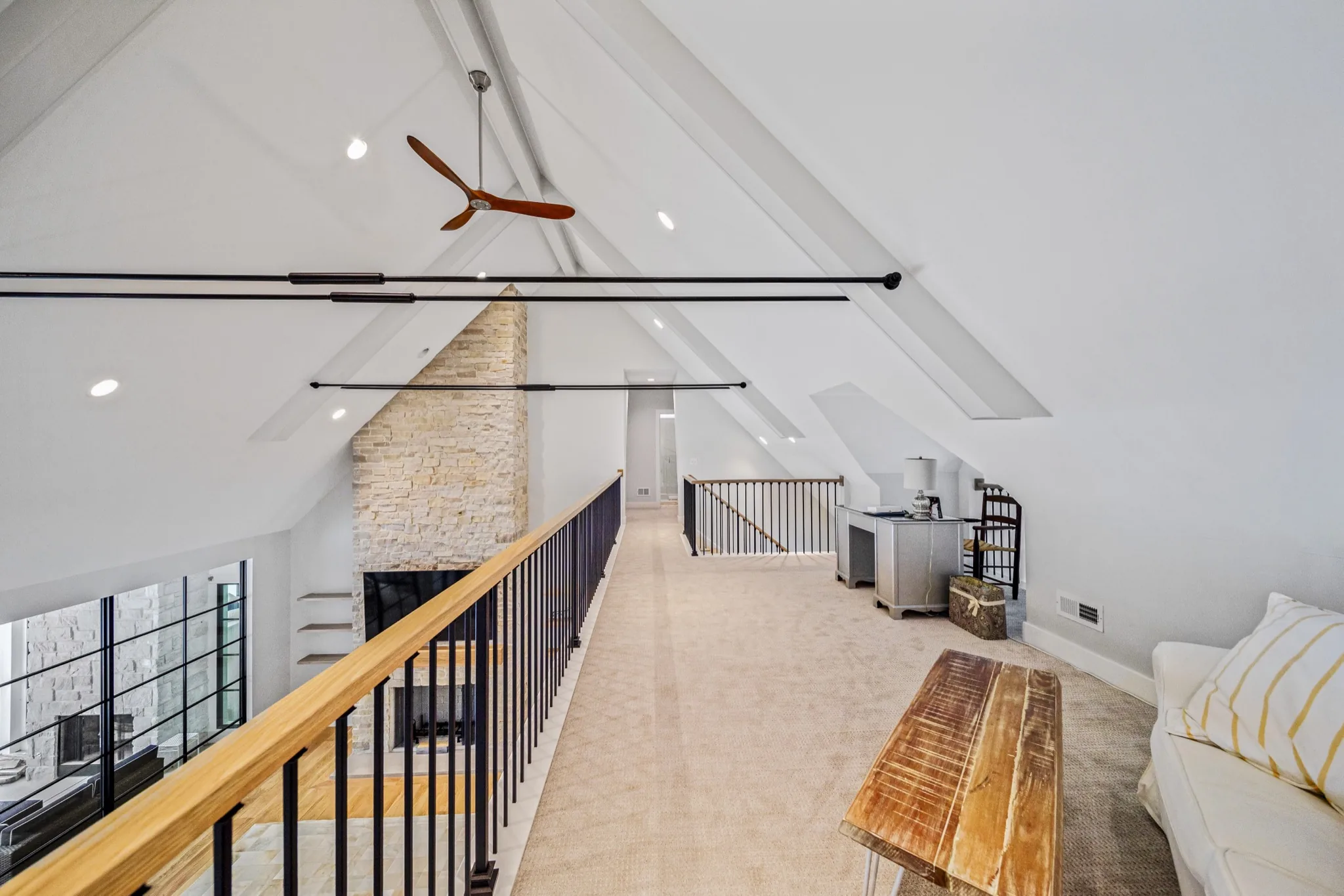 Loft walkway overlooking two-story great room with cathedral ceiling, exposed beams, stone fireplace chimney, and modern ceiling fan — luxury estate by Skoda Construction, Northeast Ohio