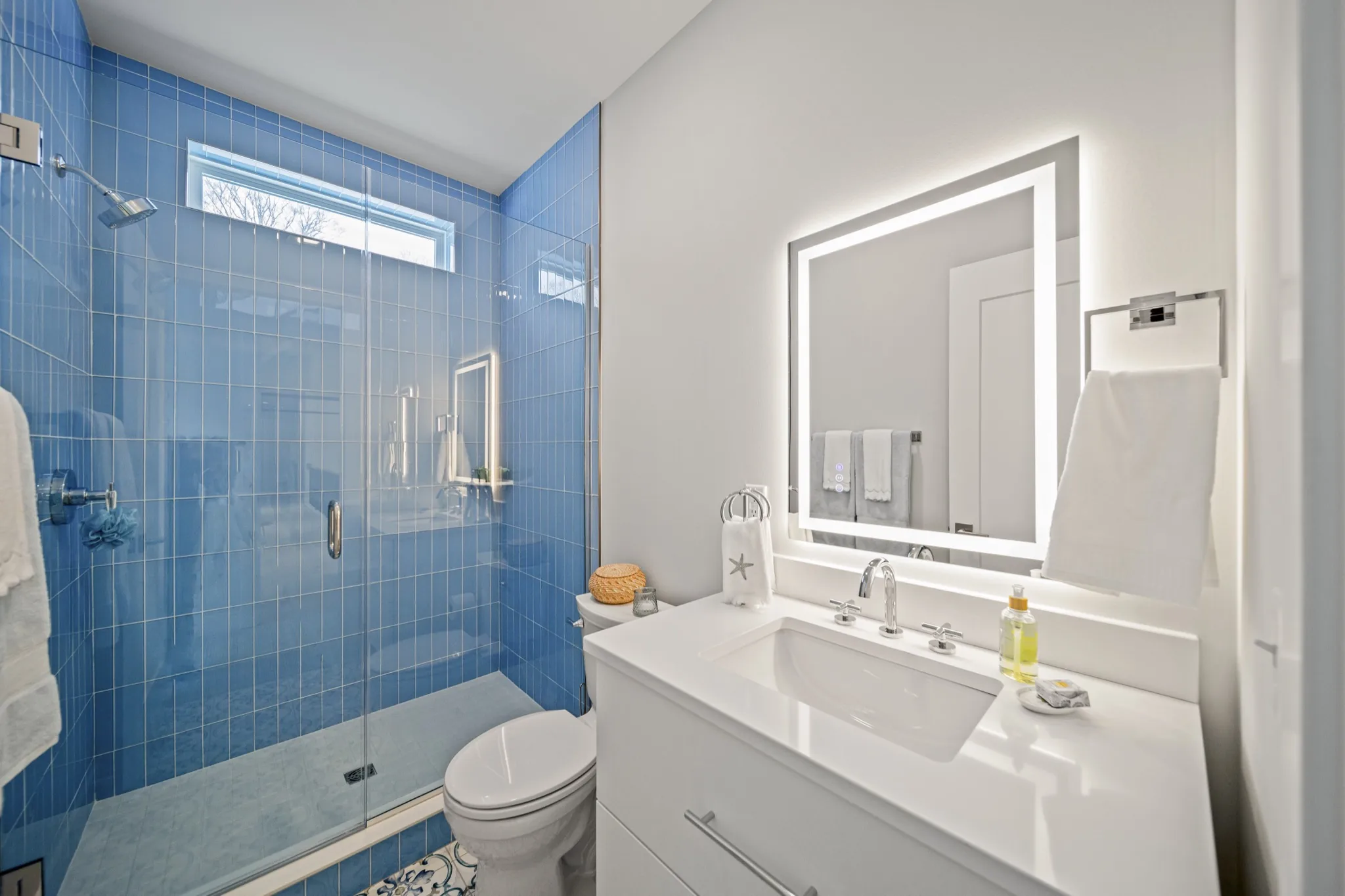 Contemporary bathroom with vibrant blue tile walk-in shower, LED-backlit vanity mirror, and mosaic tile flooring — luxury custom home by Skoda Construction, Northeast Ohio